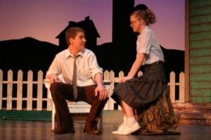 Two teenagers in high school play seated on stage.