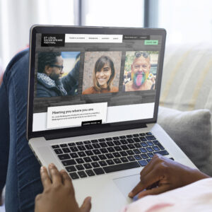 Person using a laptop while browsing the website for the St. Louis Shakespeare Festival, featuring photos of three individuals and the text "Meeting you where you are.