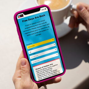 Person holding a smartphone displaying a webpage titled "Free Days Are Back" with details of in-person and virtual programs. A cup of coffee is on the table in the background.