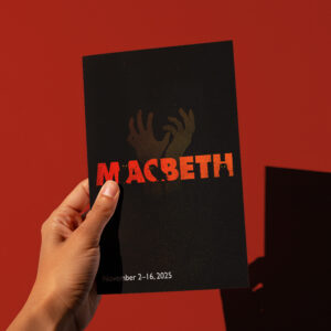 A hand holds a black Macbeth flyer with red and yellow text, shadowy hands in the background, and dates November 2-16, 2025 at the bottom.