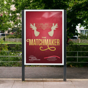 A red poster for "The Matchmaker" by Hudson Valley Shakespeare features white gloved hands holding a geometric heart, displayed at a bus stop with greenery in the background.