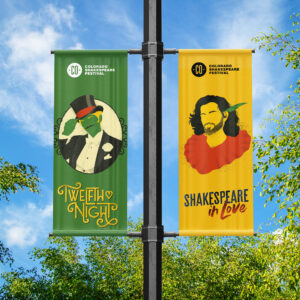 Two vertical banners for the Colorado Shakespeare Festival hang on a pole; one advertises "Twelfth Night" and the other "Shakespeare in Love" against a backdrop of trees and blue sky.