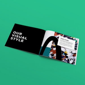 An open booklet on a green surface displays "OUR VISUAL STYLE" on the left page and a colorful abstract design with a "Style Guide" section on the right page.