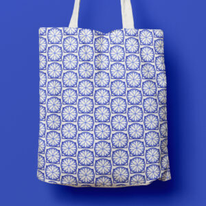 A white tote bag with a blue geometric floral pattern, hanging against a solid blue background.